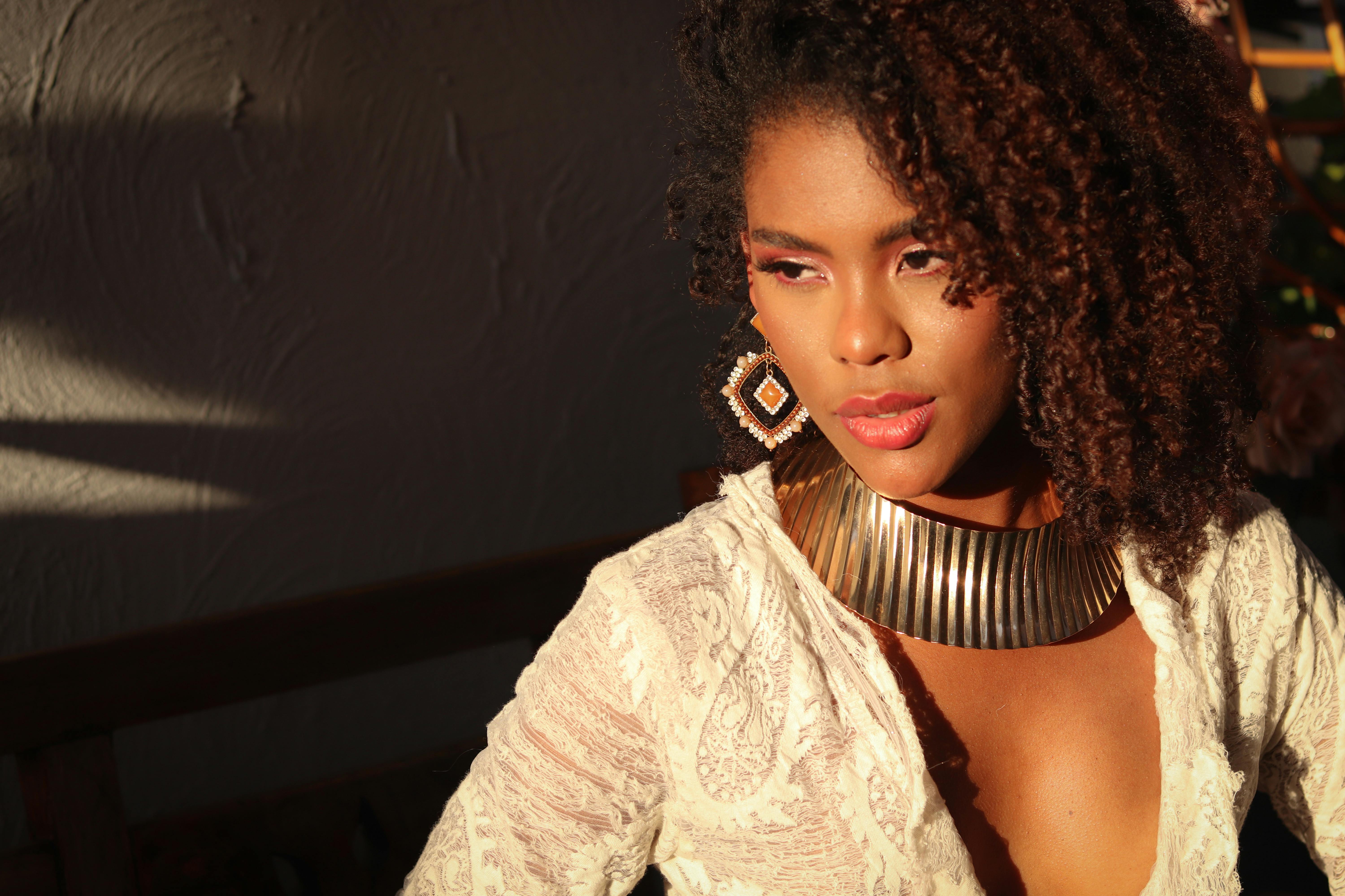 Elegant portrait of a woman in warm sunlight wearing a gold necklace and lace attire.