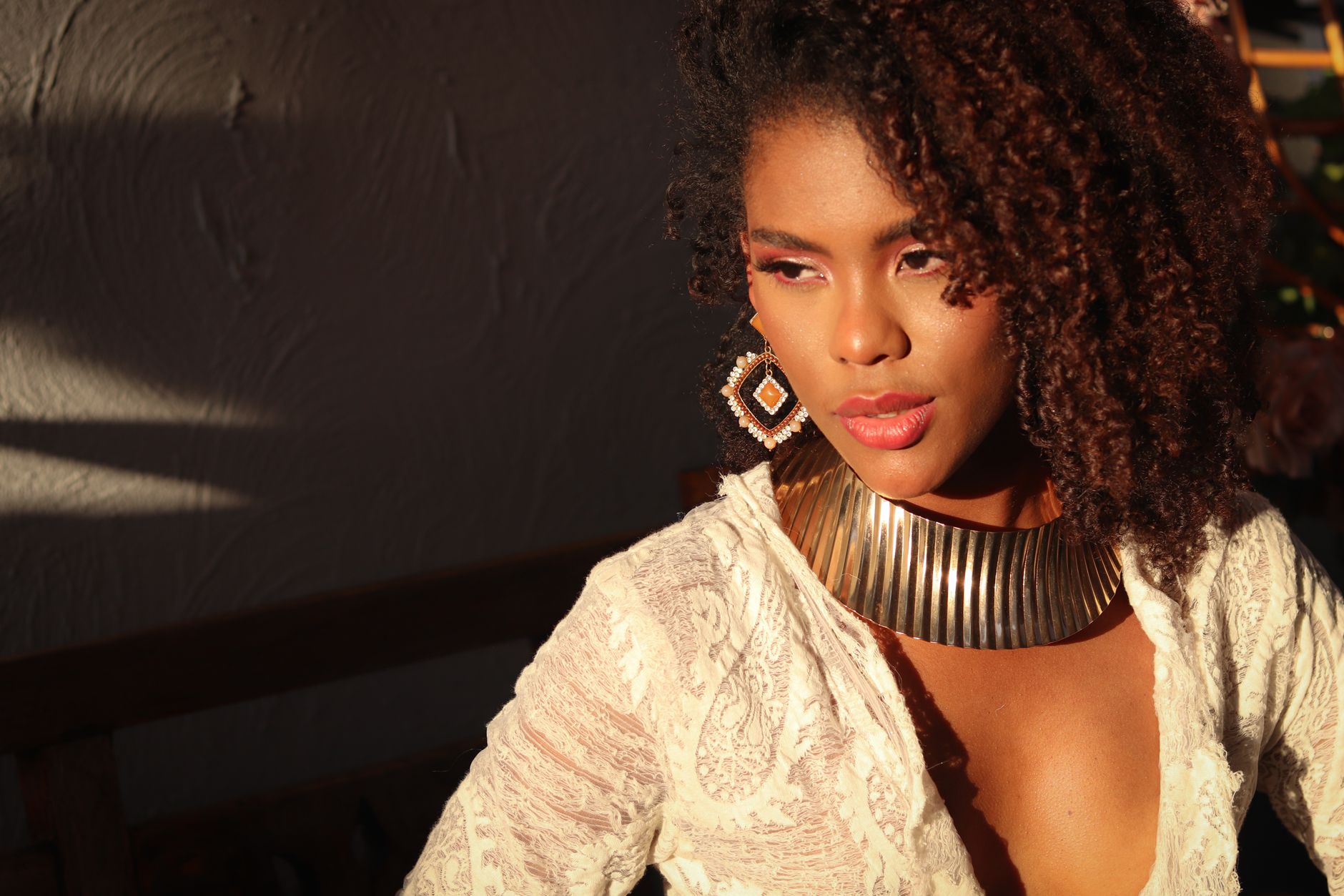 Elegant portrait of a woman in warm sunlight wearing a gold necklace and lace attire.