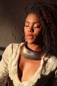 A woman in lace attire with closed eyes, bathed in warm sunlight indoors.
