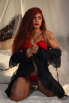 Sensual boudoir photo of a woman in red lingerie and black sheer robe on a bed.