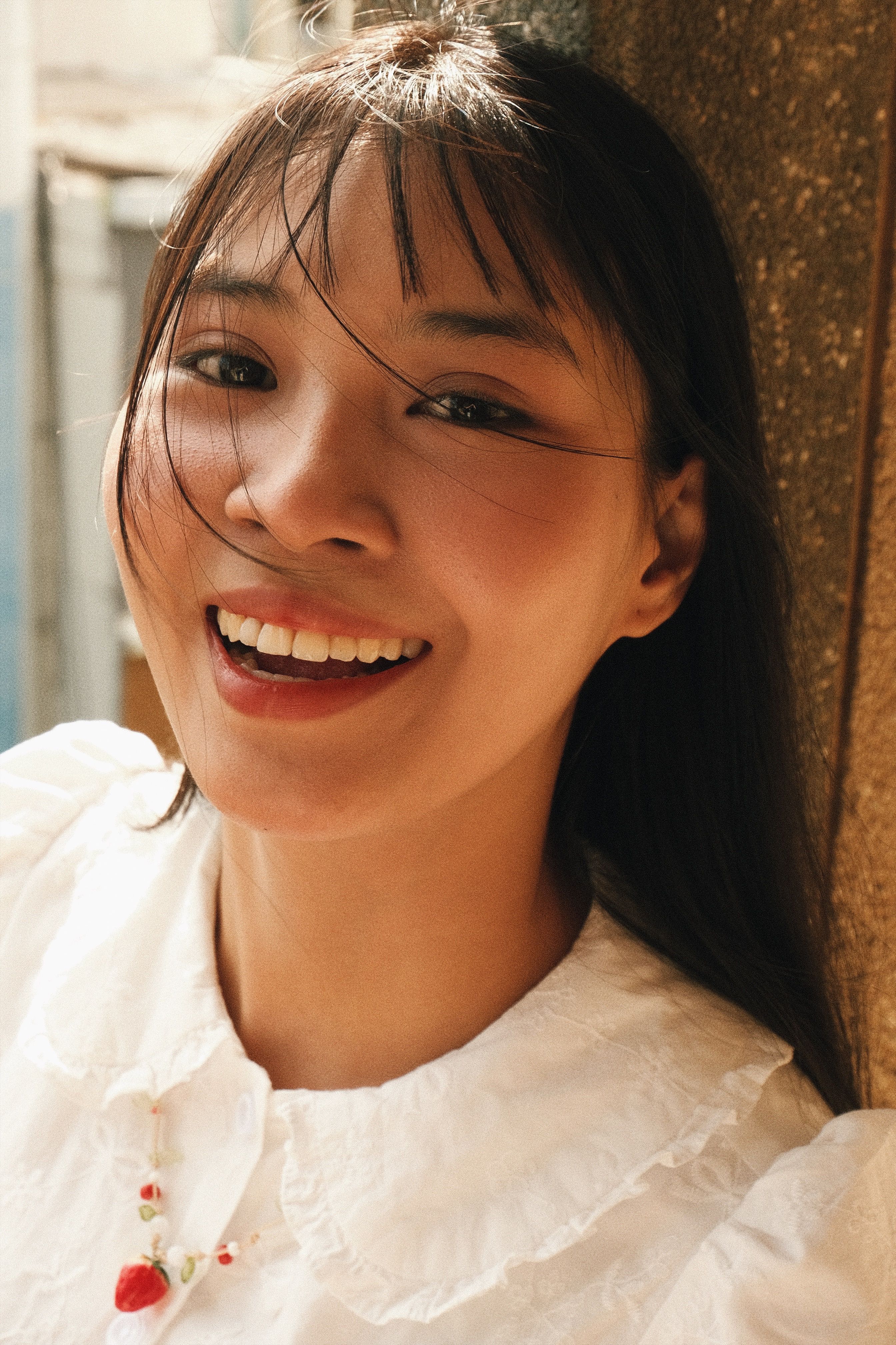 Joyful woman with long hair in sunlight, wearing a white blouse. Natural and radiant.