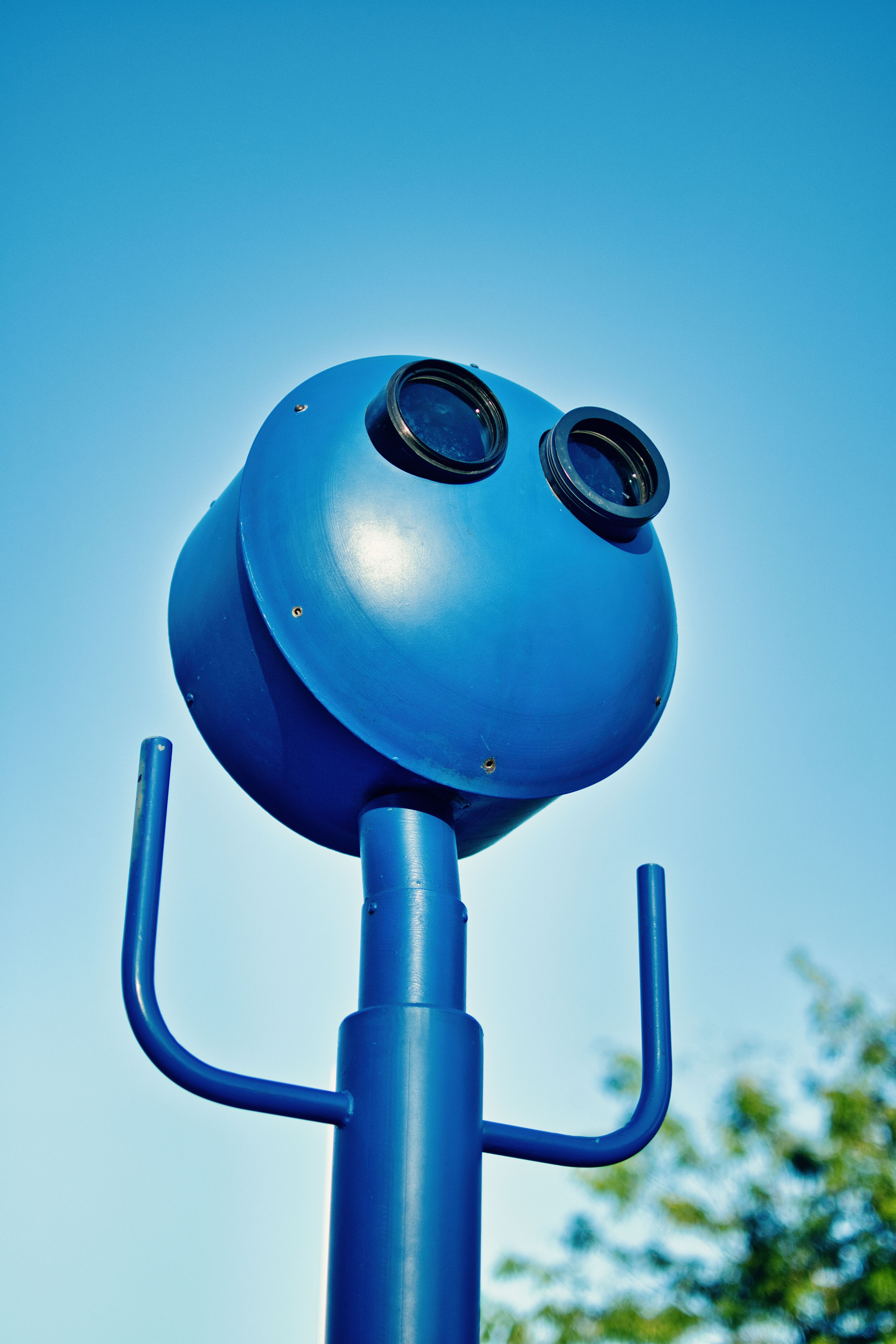 Close-up of blue binoculars set against a clear sky with lush foliage, capturing a vibrant outdoor scene.