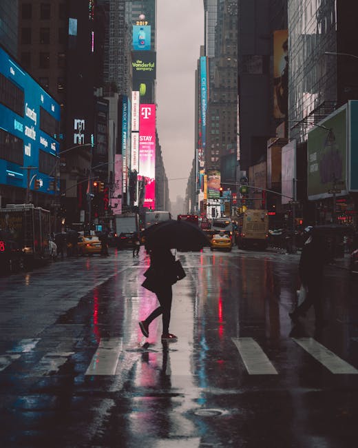 A person with an umbrella crossing Times Square at night, reflecting neon lights.
