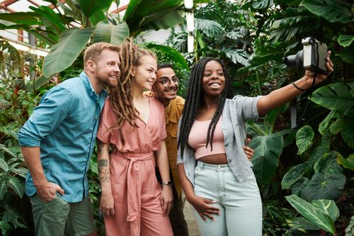 Free Group of diverse friends taking a selfie among lush greenery in a greenhouse. Vibrant happiness and togetherness. Stock Photo