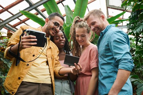 Free A diverse group of friends smiling and viewing a Polaroid instant photo together outdoors. Stock Photo