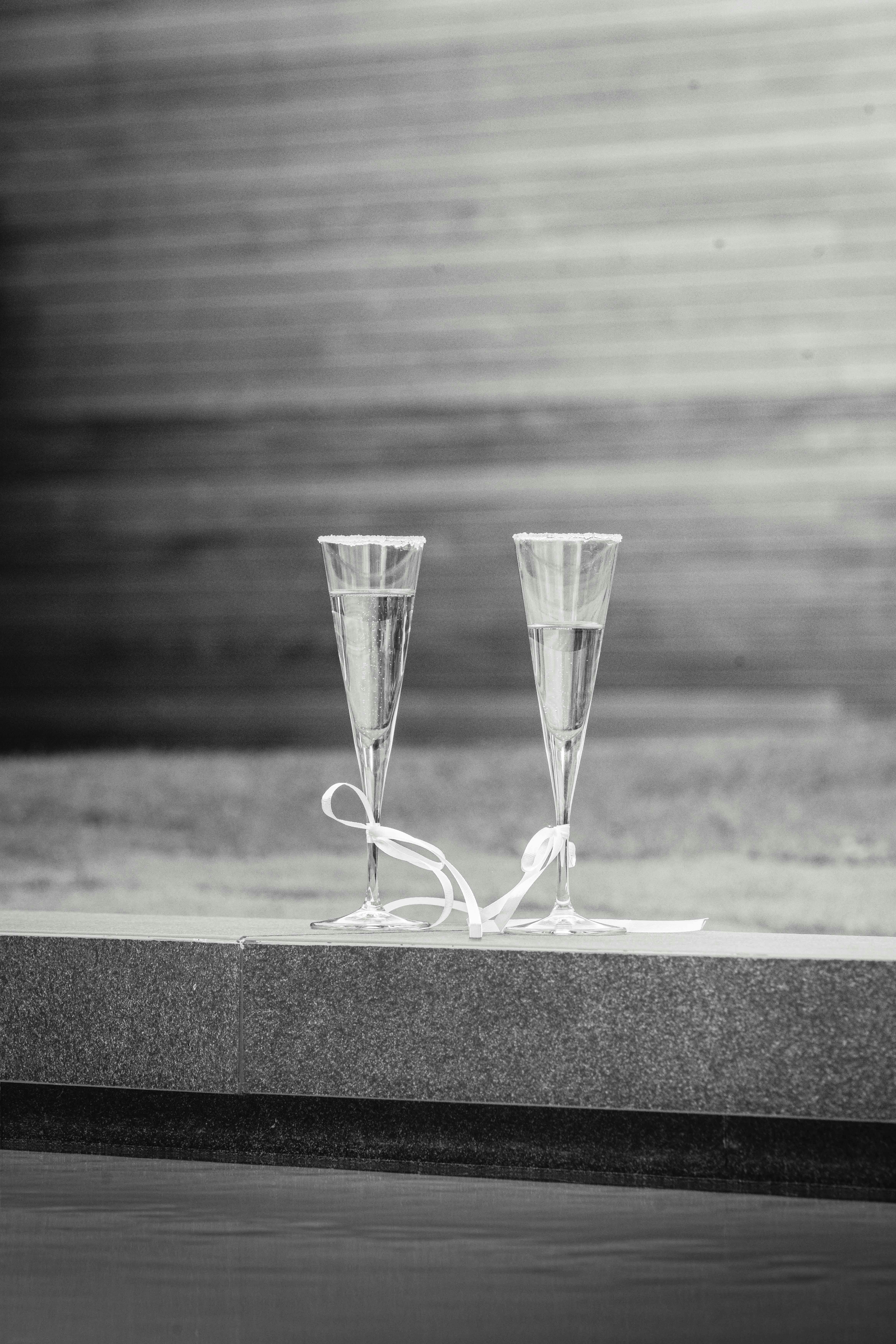 Gratis Elegante fotografía en blanco y negro de dos copas de champán atadas con una cinta sobre una encimera de piedra. Foto de stock