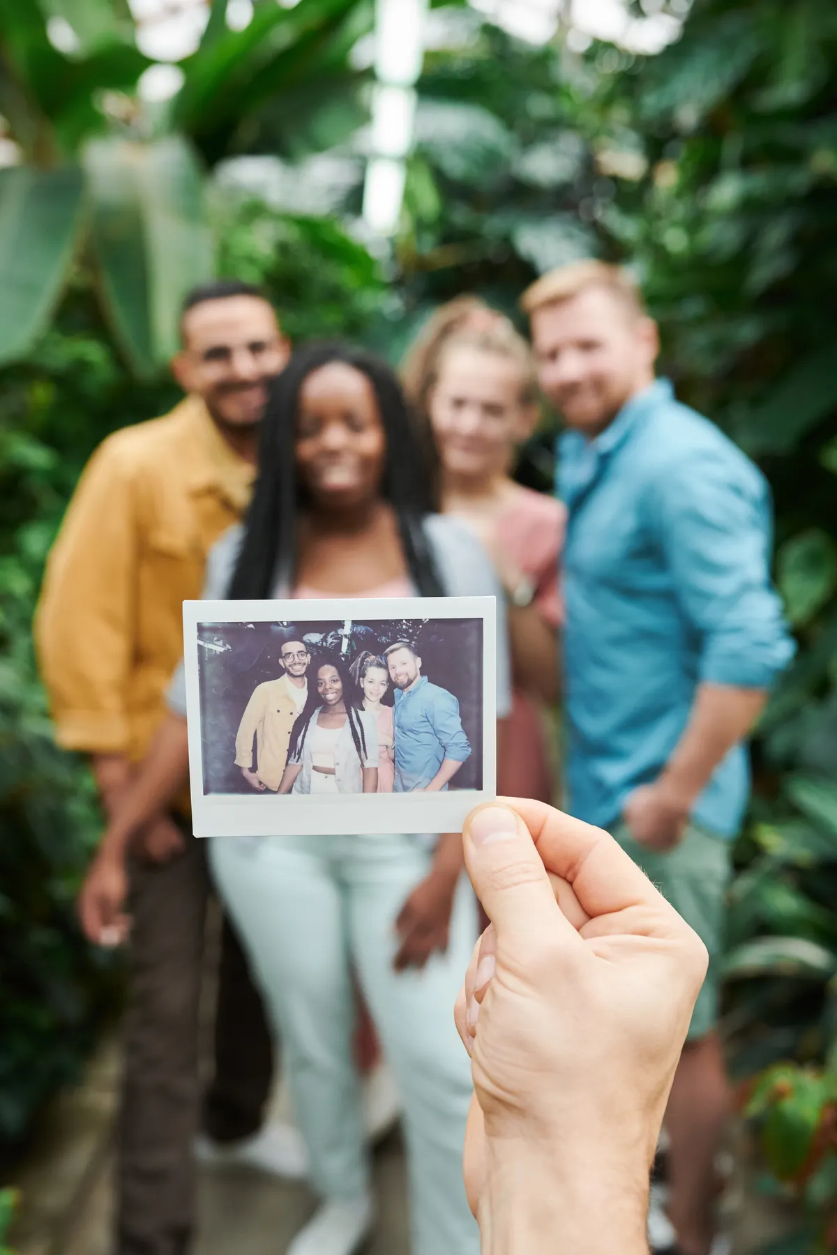 Sekelompok sahabat memegang foto polaroid bersama di taman tropis mengabadikan kenangan persahabatan