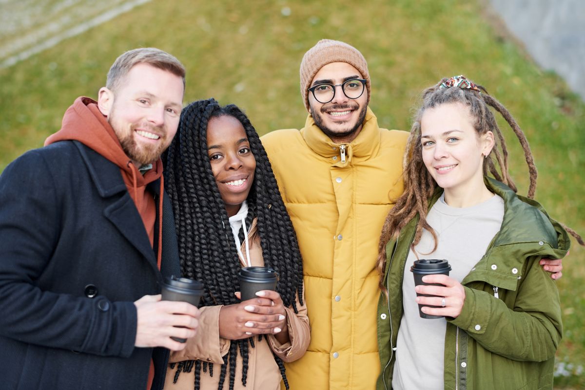A diverse group of smiling friends holding coffee cups outdoors, celebrating connection and community