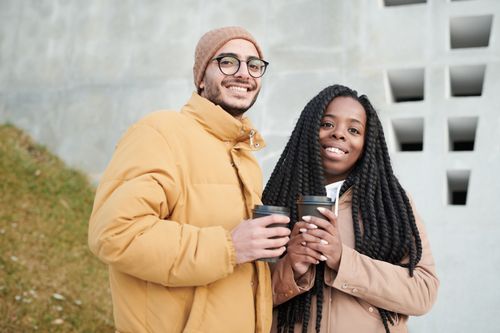 Free Smiling couple holding coffee cups outside on a cool day, dressed in warm jackets. Stock Photo