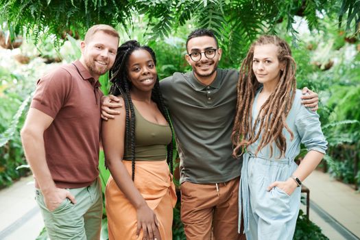 A group of four smiling friends standing together in a green garden, showcasing diversity and friendship.