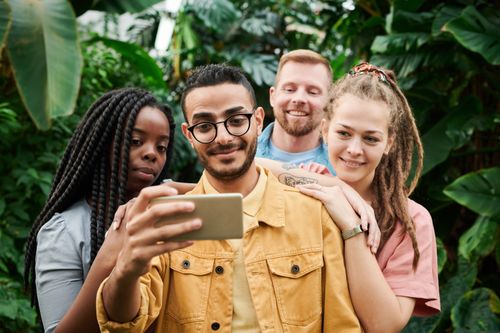 Free A group of four friends happily taking a selfie amidst lush greenery, capturing their joyful moments together. Stock Photo