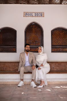 Stylish couple in elegant attire seated at a pool deck, showcasing modern fashion.