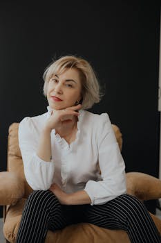 Stylish woman in white blouse and striped pants sitting confidently on a chair.