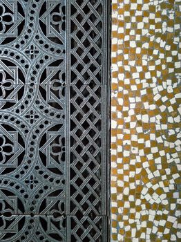 Close-up of a detailed metal grille and mosaic tile pattern displaying artistic contrast.