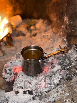 Metal coffee pot brewing on open fire, showcasing rustic outdoor cooking experience.