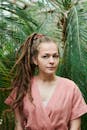 一名梳着辫子的女子身着粉色服装，在户外葱郁的植物间摆好姿势