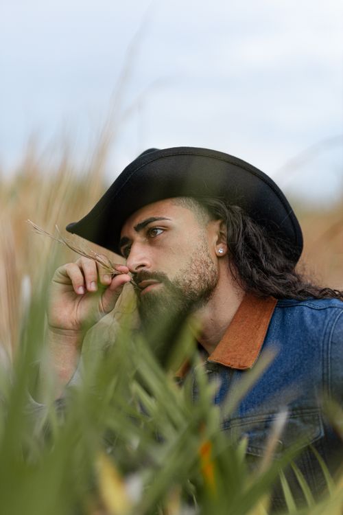 Free Portrait of a man with a cowboy hat in a field, blending rustic charm with modern style. Stock Photo
