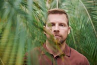 一名留着胡须的男子站在绿叶后面，肖像以景深拍摄