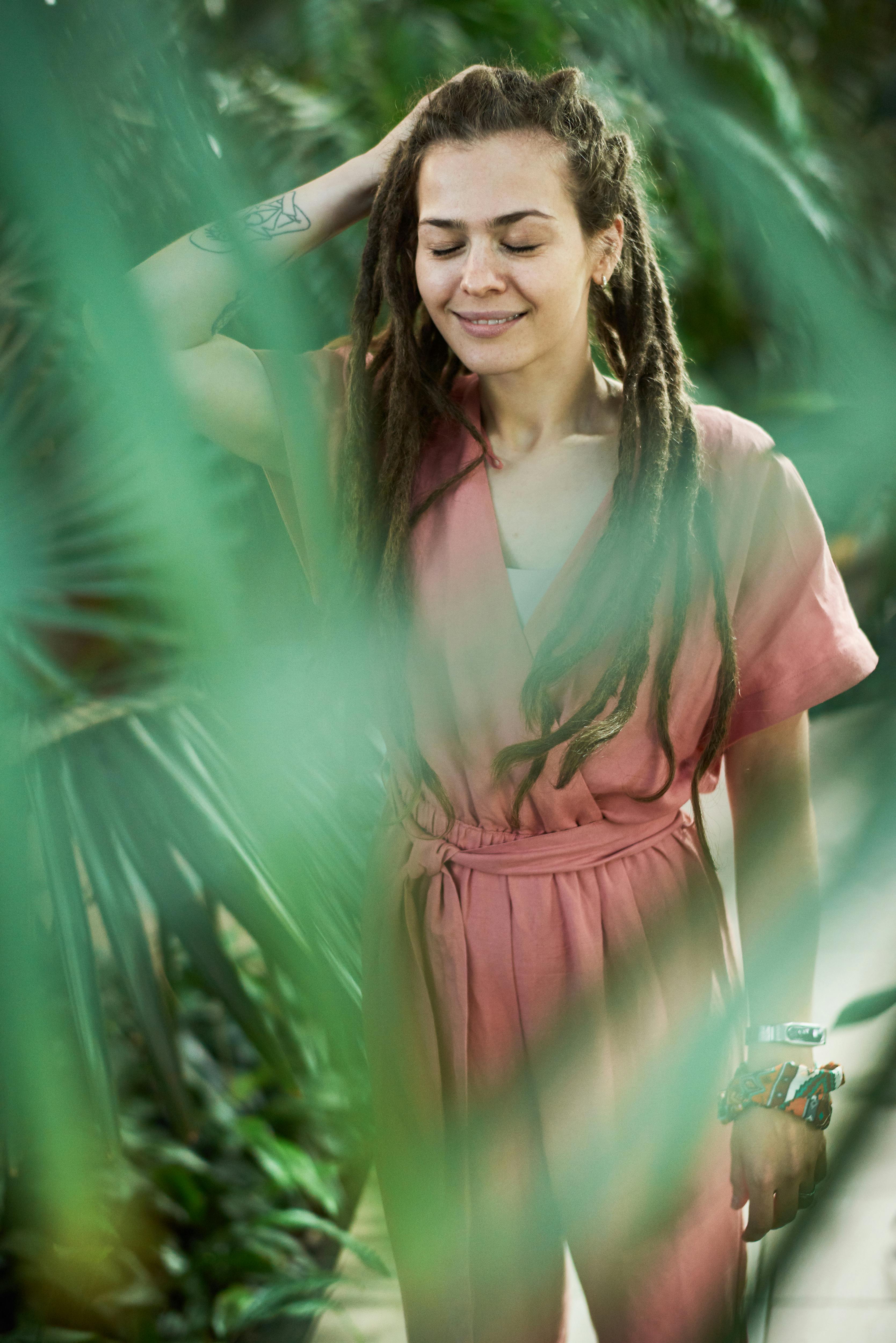 A happy woman with dreadlocks enjoys a moment surrounded by lush tropical greenery.