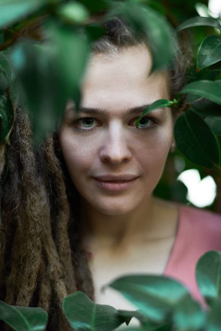 Close-up portrait of a woman surrounded by lush green leaves, creating a serene and natural atmosphere.