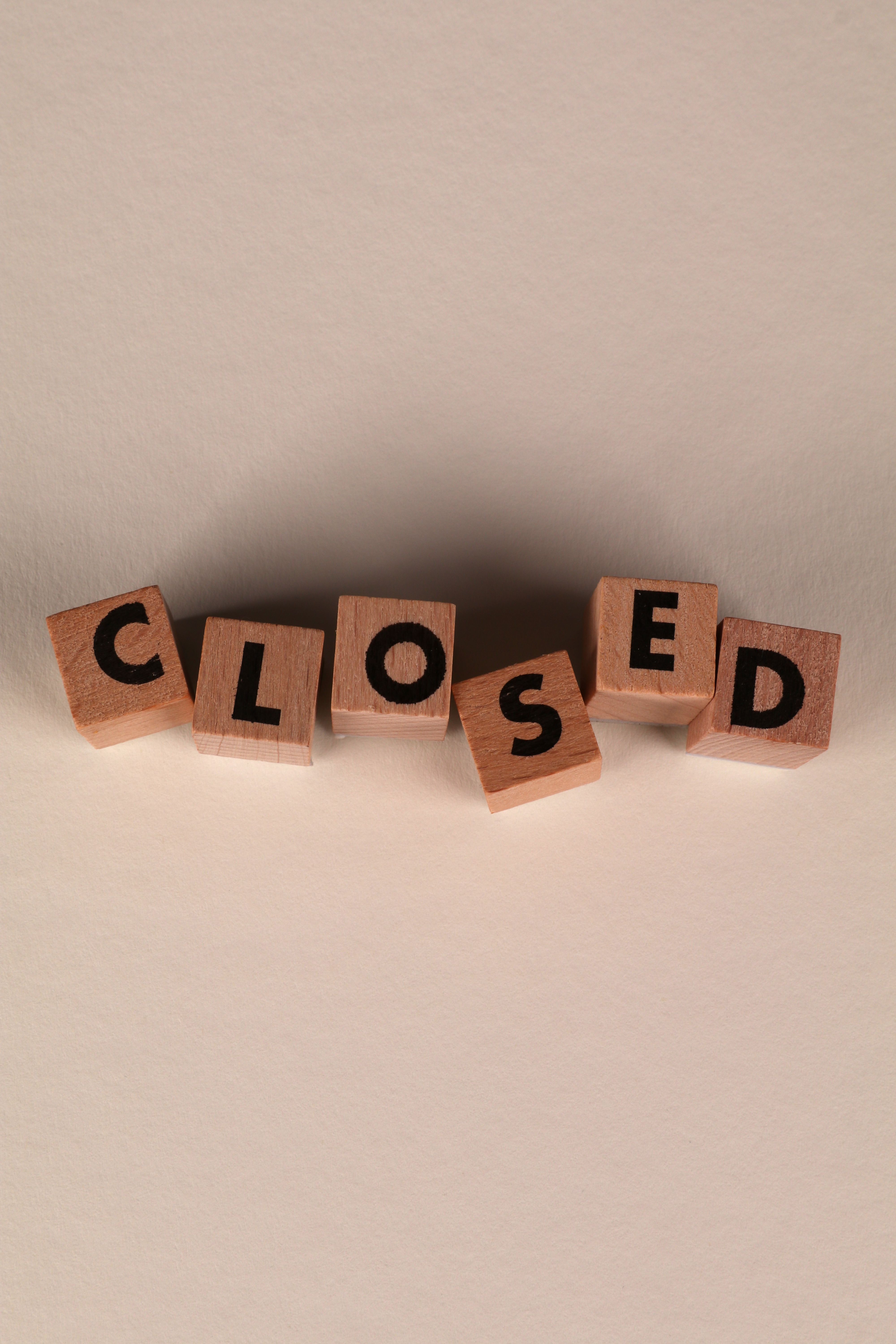 Wooden blocks arranged to spell 'CLOSED' on a beige background, conveying closure.