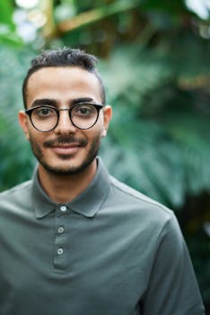 绿色背景前，一位戴着眼镜、穿着马球衫的男子微笑着的肖像