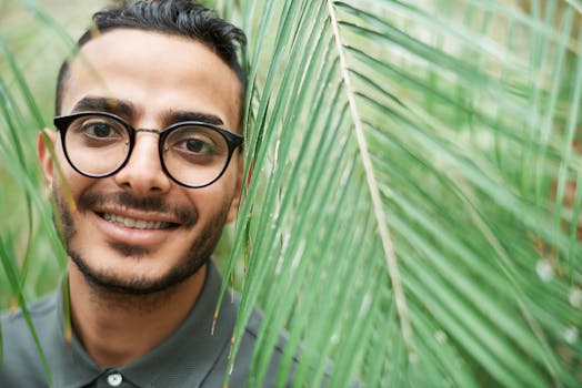 特写肖像中，一位戴眼镜的男子面带微笑，部分被绿叶遮挡，传递出温暖的感觉