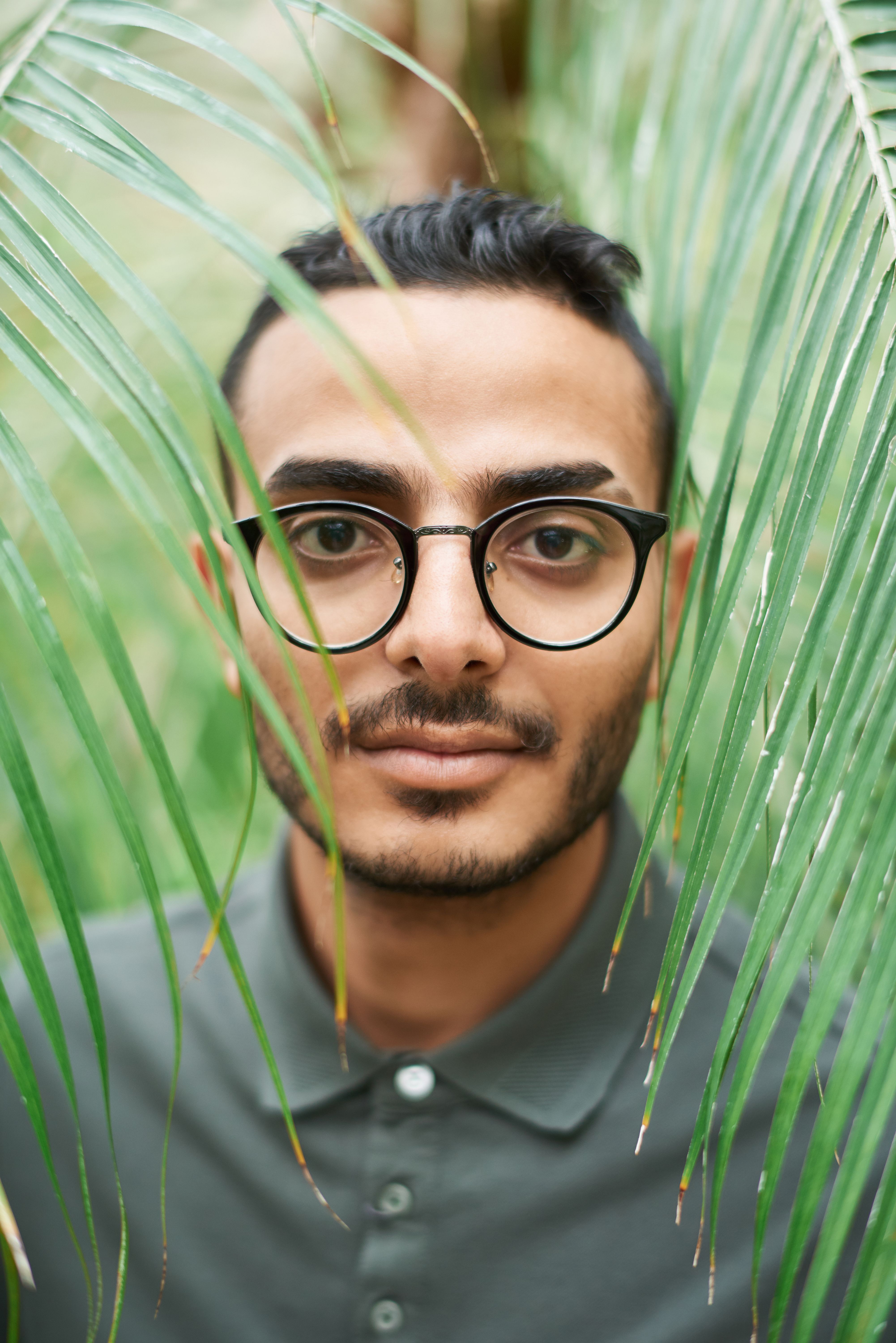 Close-up portrait of a man with eyeglasses surrounded by green leaves, creating a natural frame.