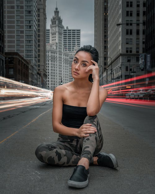 Photo of Woman Sitting on Road With Light Streaks of Vehicles