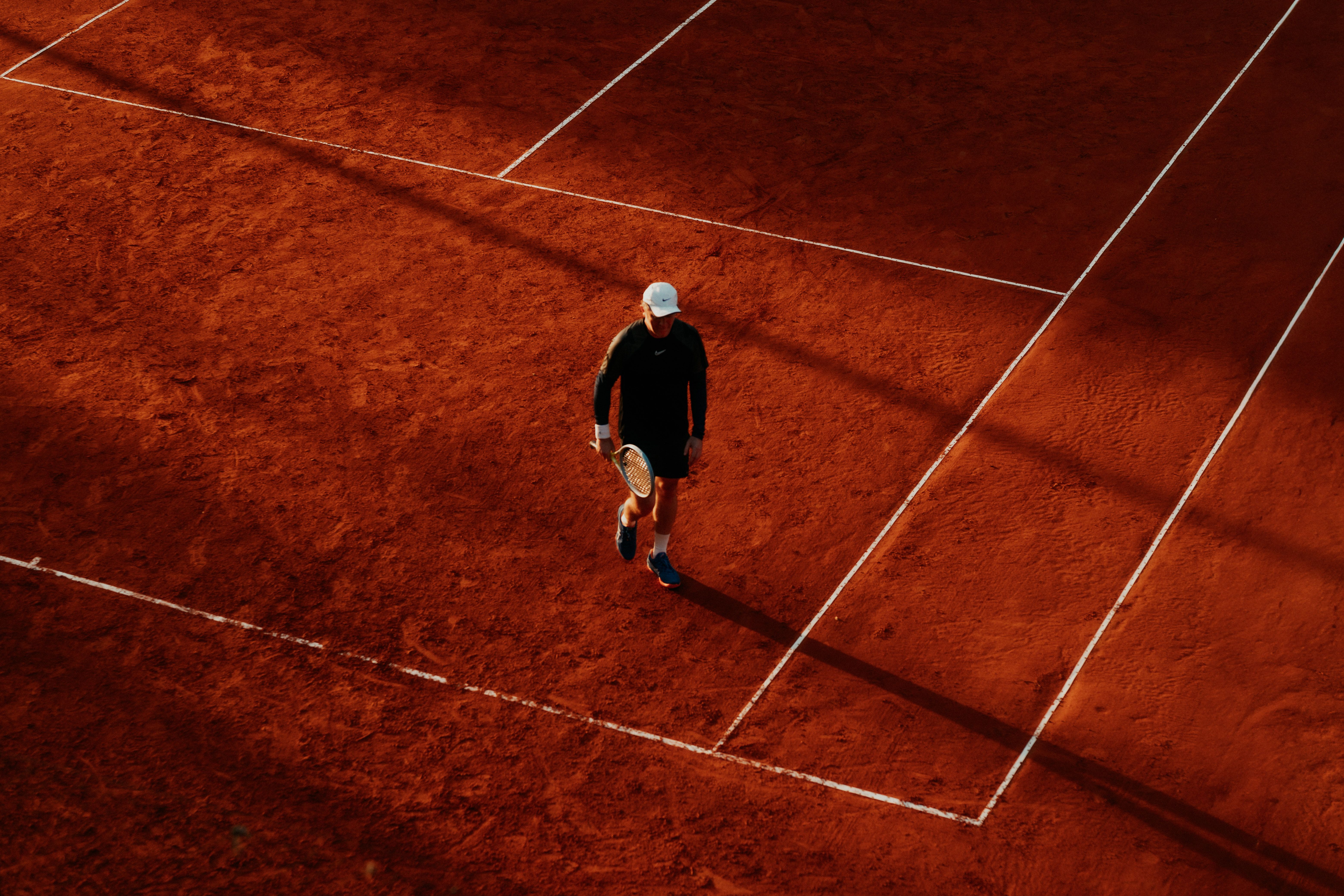 Tennis photo featuring An overhead shot of a tennis player on a clay court during the day, with long shadows.