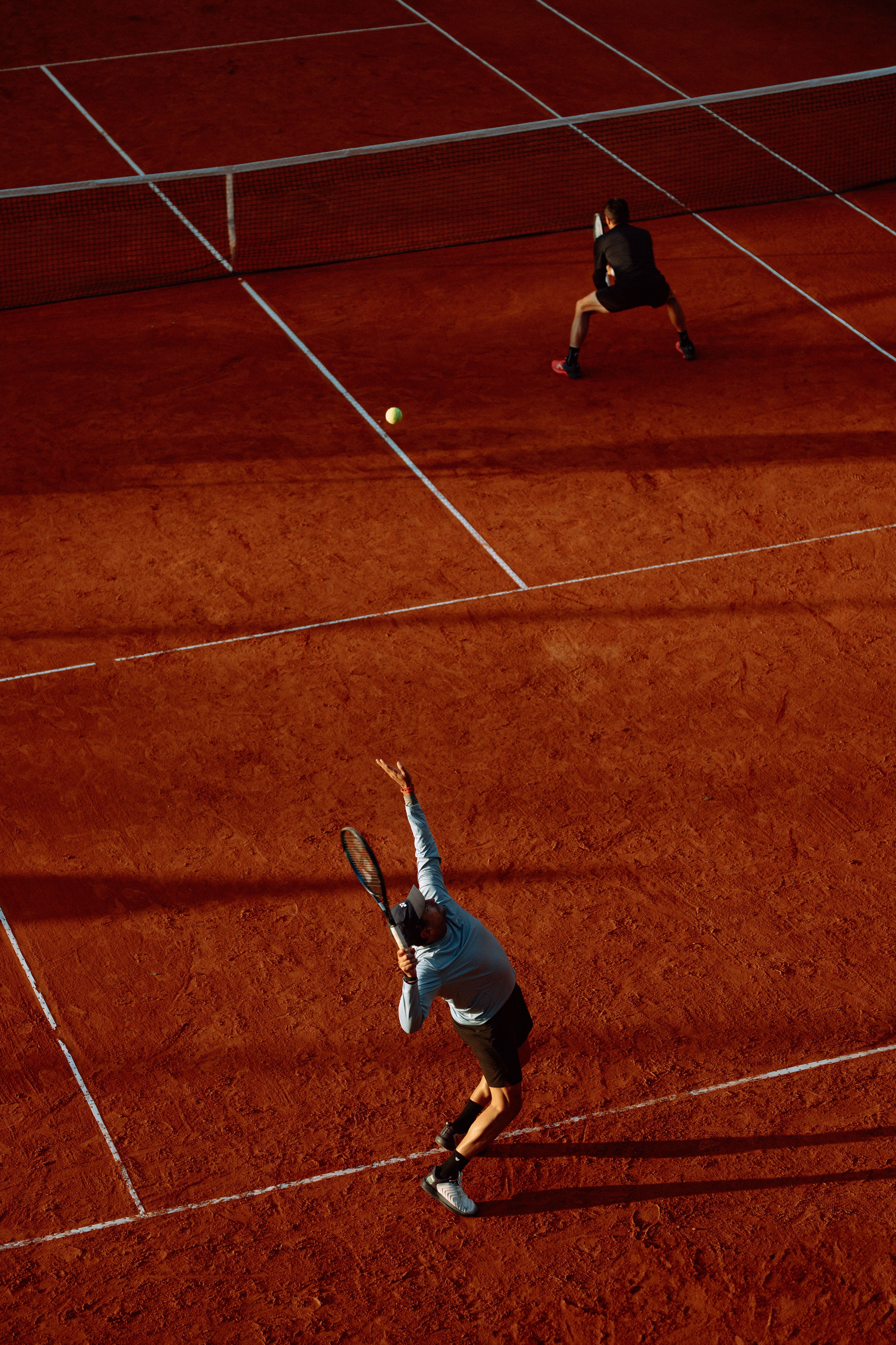 Overhead view of an intense tennis match on a clay court with dramatic shadows