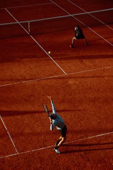 Overhead view of an intense tennis match on a clay court with dramatic shadows