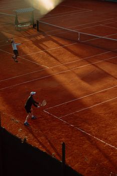 High-angle view of an active tennis game on a clay court during sunset, capturing dynamic play.