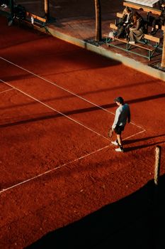 A lone tennis player stands on a sunlit clay court, capturing a serene moment of the sport.