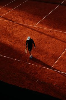 A lone tennis player with a racket on a clay court, captured in a dramatic aerial view.