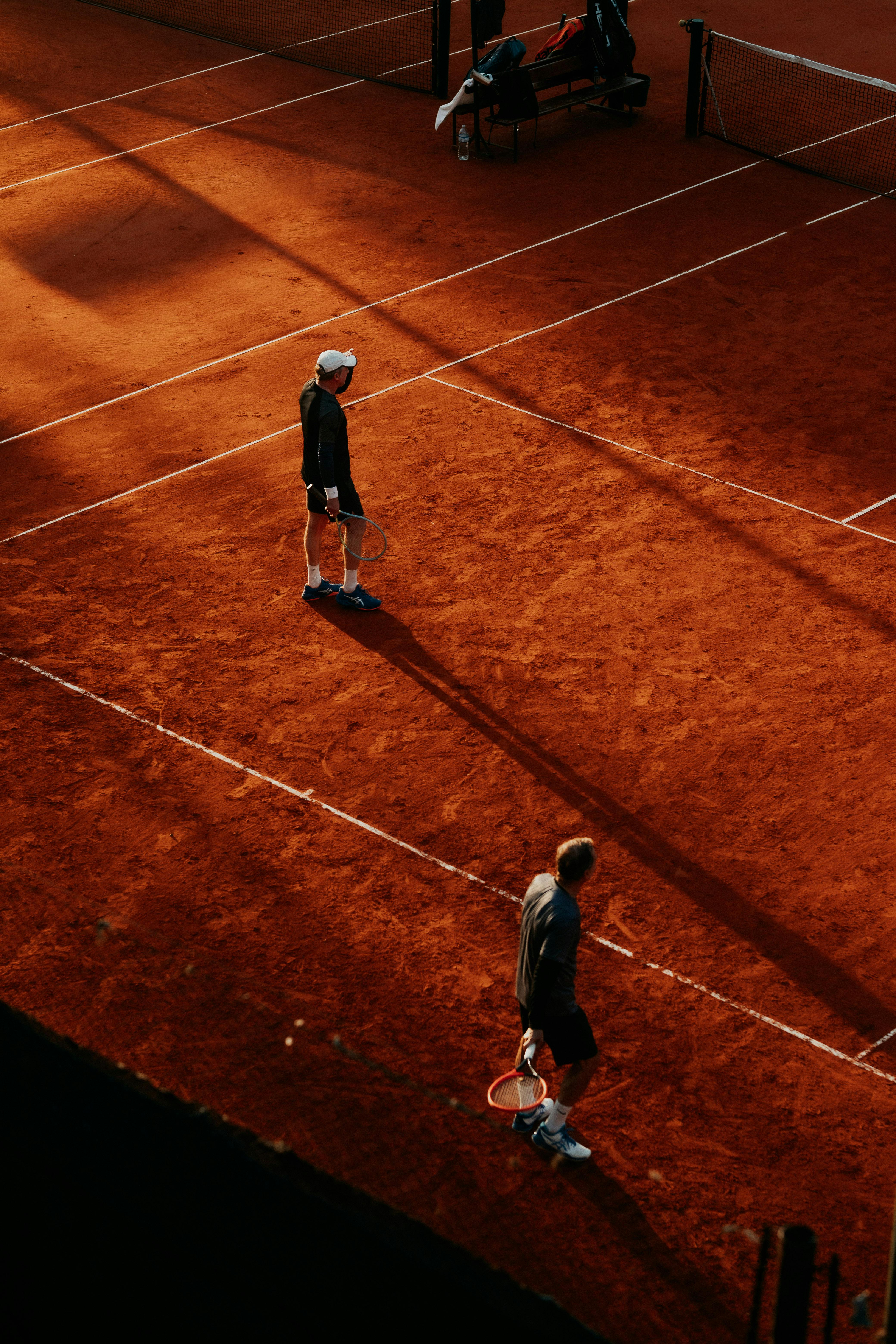Two players compete on a clay tennis court under warm, dramatic sunset lighting.