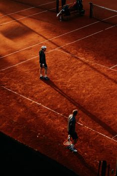 Two players compete on a clay tennis court under warm, dramatic sunset lighting.