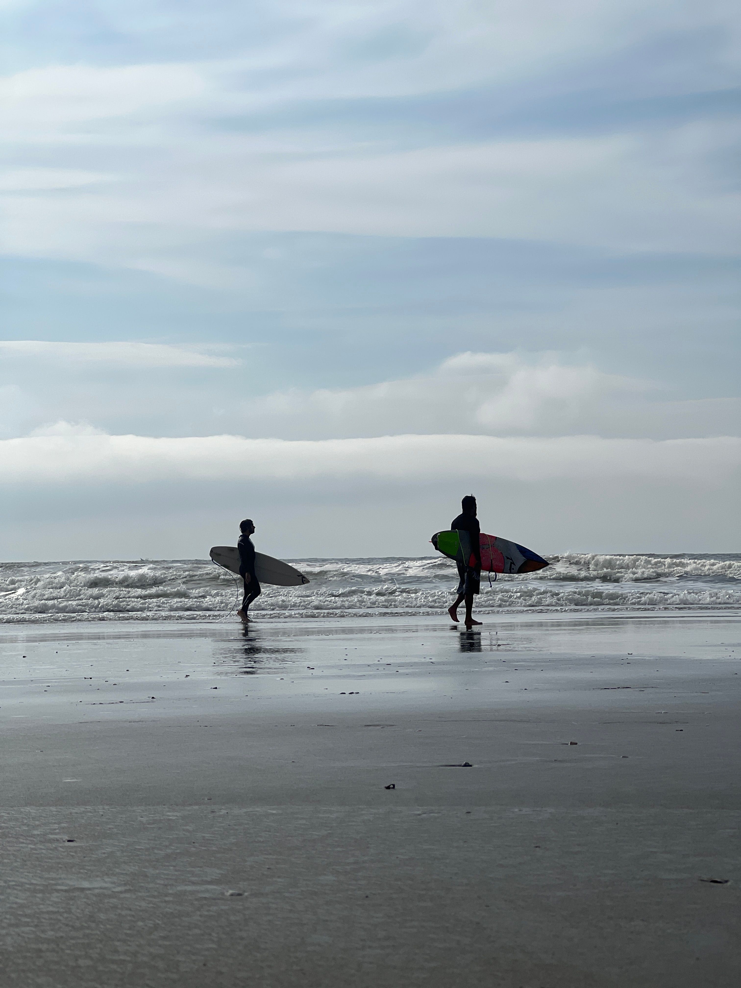 Two surfers walking the shoreline with boards — photo by Wladimir Roge on Pexels