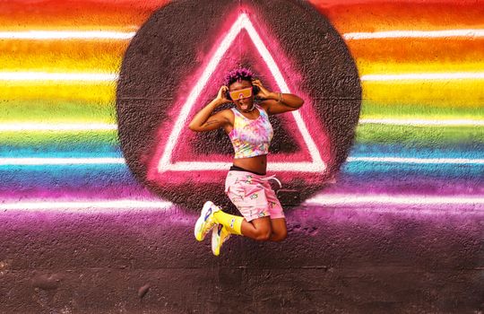 Vibrant image of a joyful woman jumping in front of a rainbow mural in Atlanta, Georgia.
