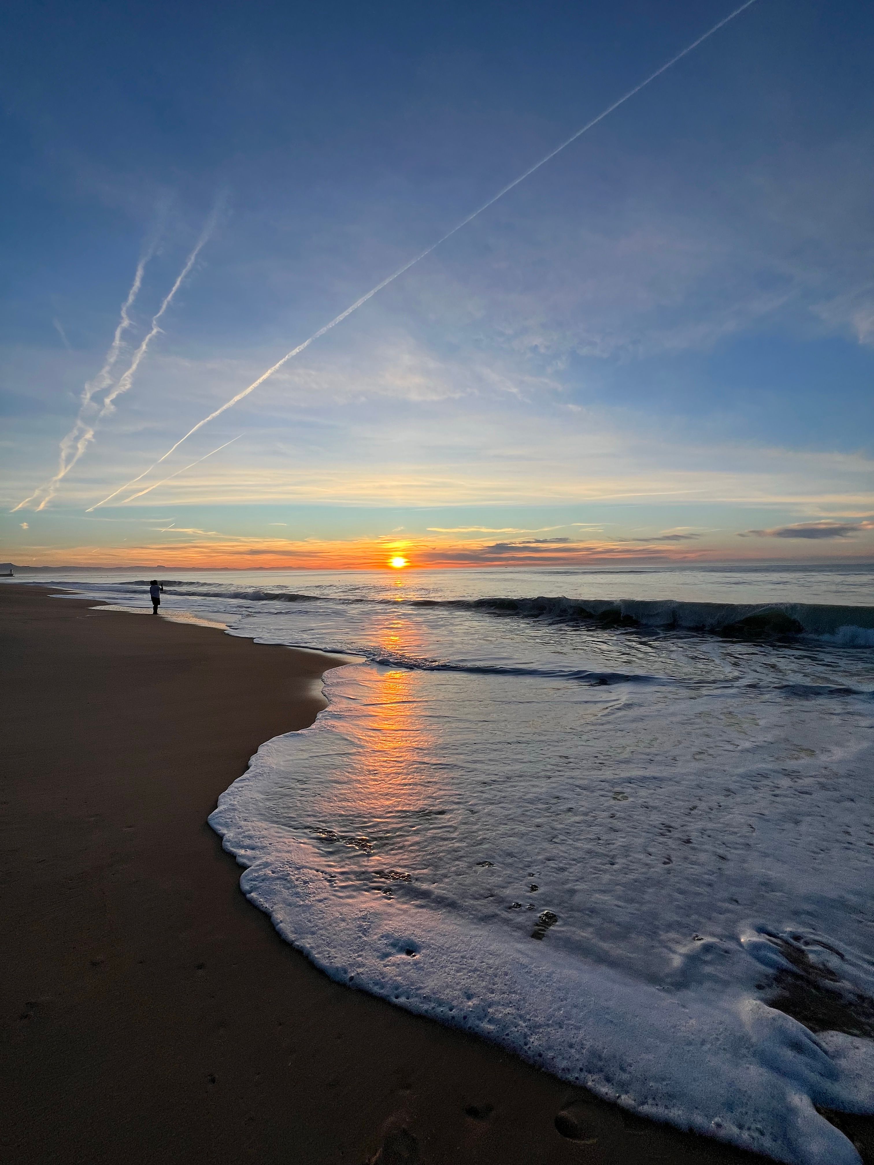 A romantic beach scene at sunrise with a couple walking on the shore.