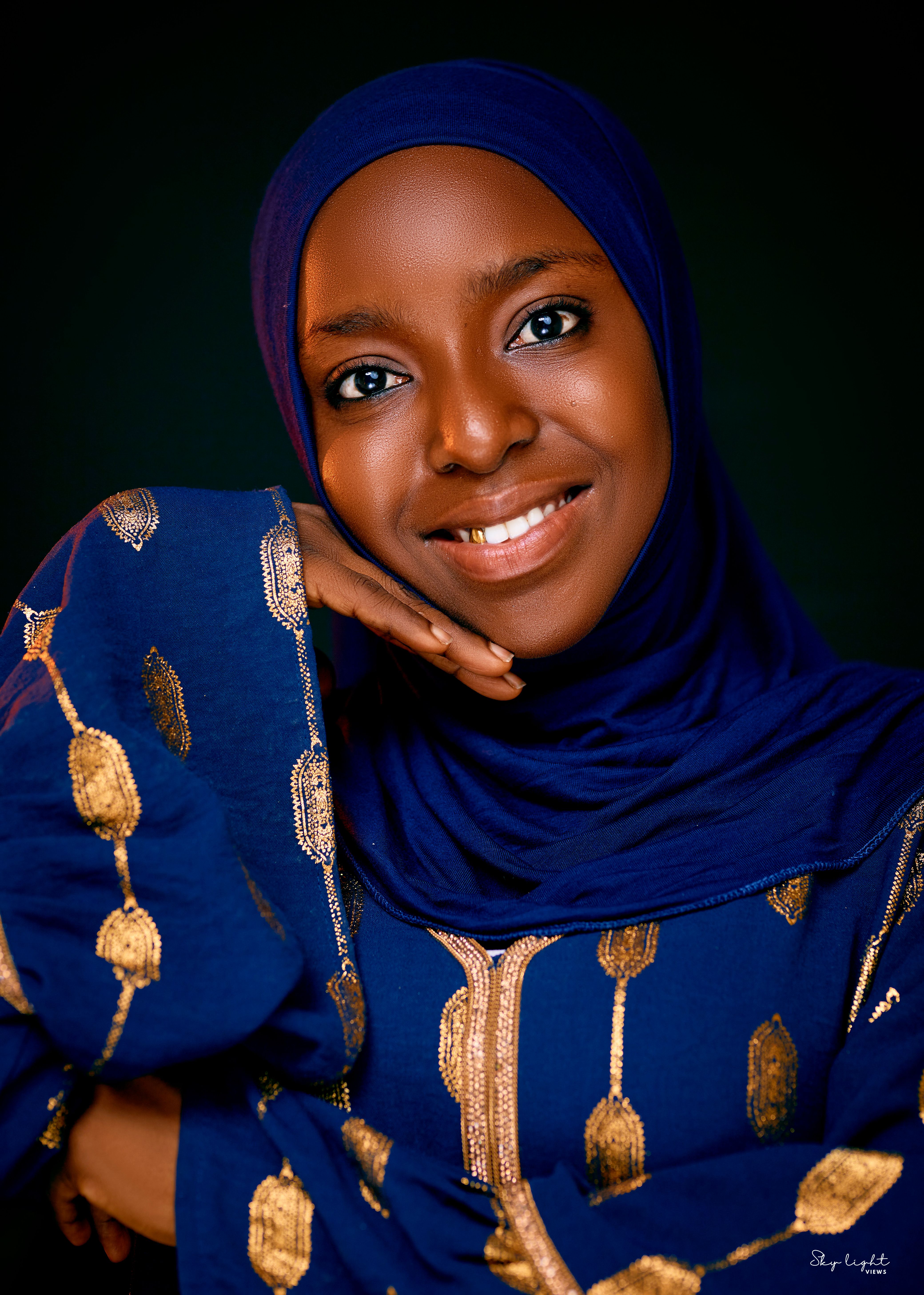 A woman dressed in vibrant blue traditional attire smiles warmly, showcasing her cultural heritage.