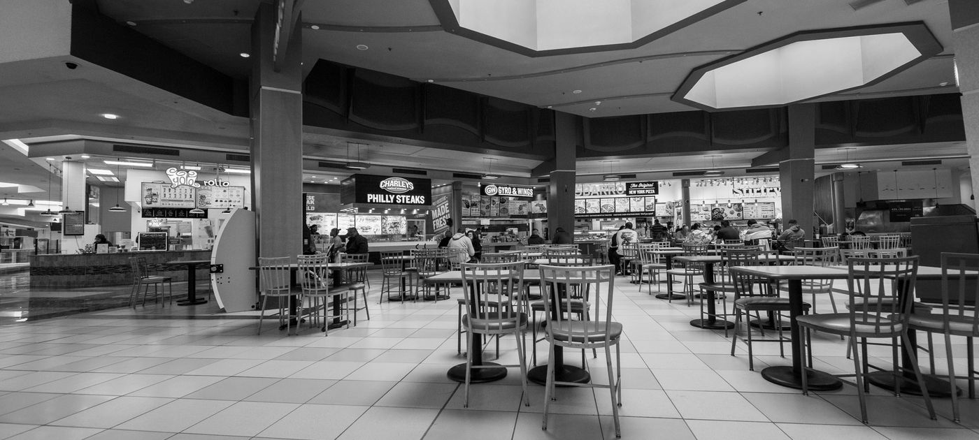 Food court seating with fast food outlets behind — multi-outlet F&B groups need synchronised cockroach treatment across every branch