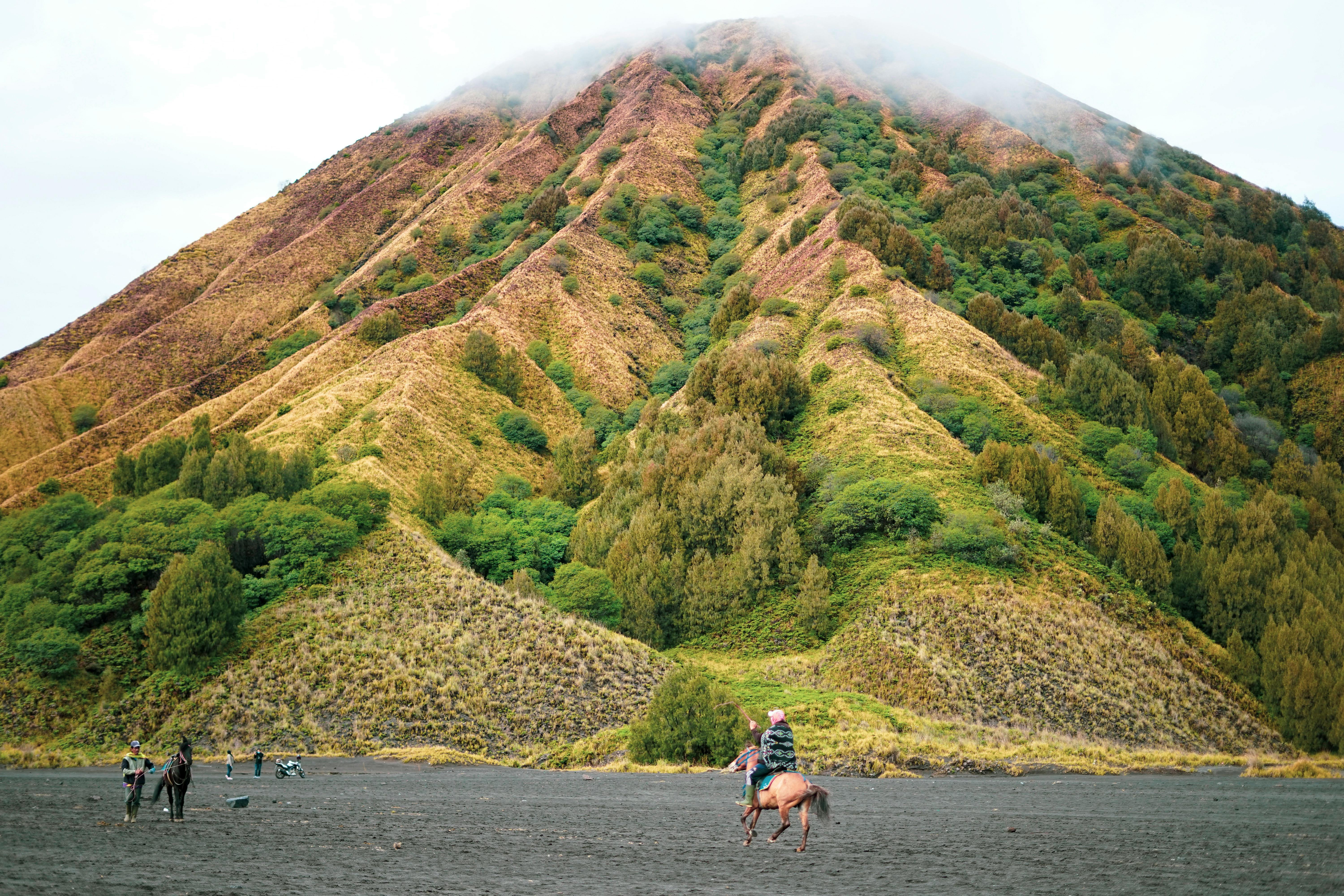 A rider on horseback traverses the sandy base of Mount Bromo, East Java.