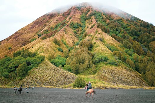 A rider on horseback traverses the sandy base of Mount Bromo, East Java.