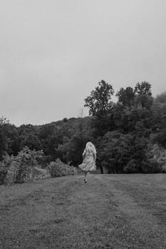 A woman in a dress dashes through a foggy rural landscape, creating a sense of escape and freedom.