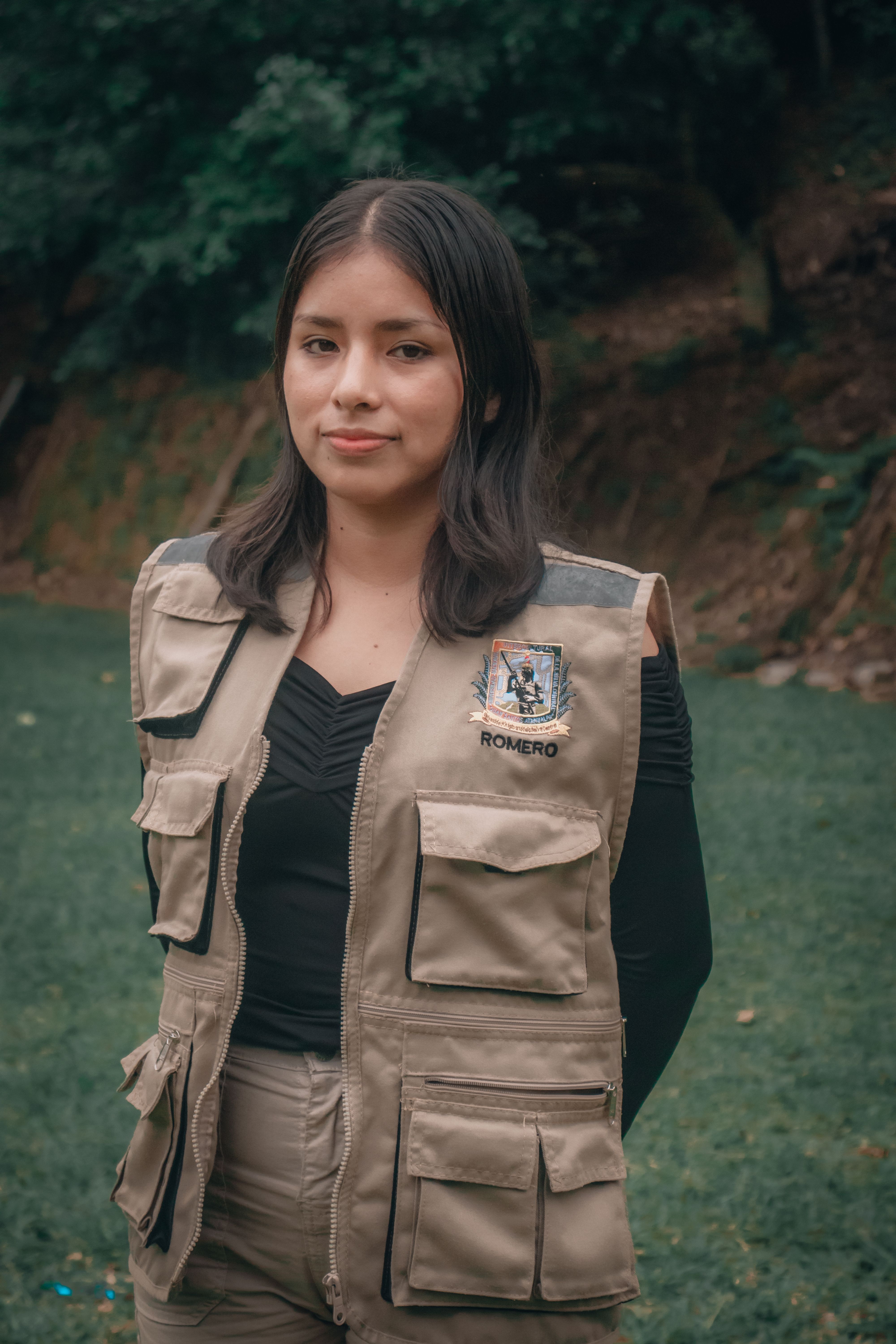 Young woman outdoors in a nature setting wearing a vest, looking at camera.