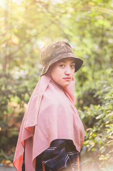 Portrait of a woman in a pink hijab and hat outdoors with soft sunlight.