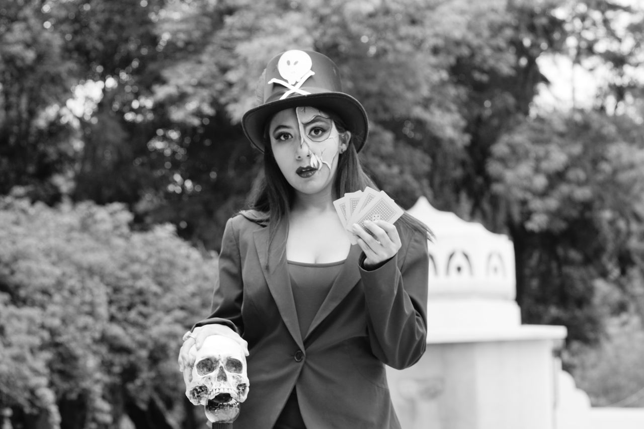 a woman in a black hat and spooky makeup holding a skull and cards in