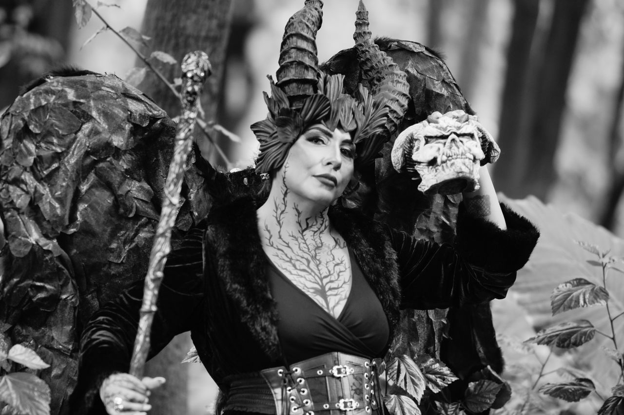 a woman in intricate fantasy costume stands in a wooded area holding a