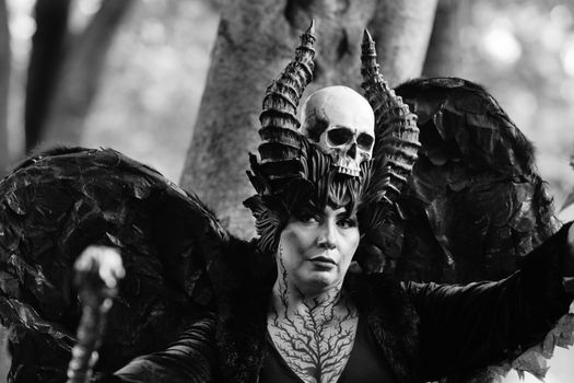 A striking black and white portrait of a person in elaborate costume with ornate skull and wings.
